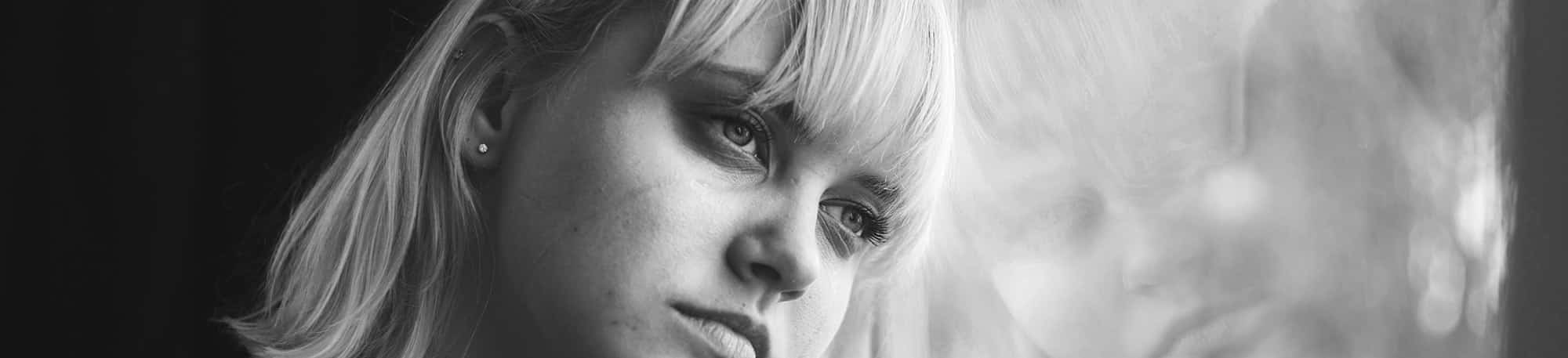 Younger, sad woman looking out the window with her head against the glass in black and white