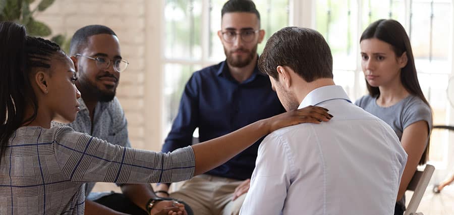 A group of peers showing support to a man as he processes his feelings during addiction treatment therapy. 