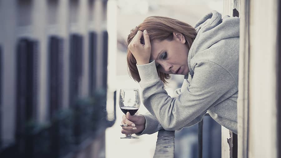 Woman with dementia holds a glass of alcohol and grabs her head while struggling to remember something shows connection between alcohol and dementia.