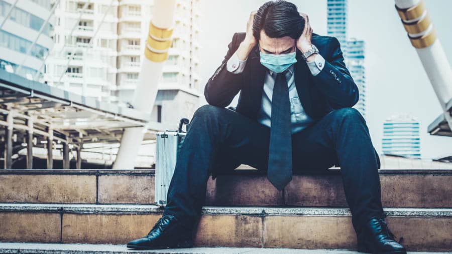 Man in a suit and covid 19 mask sitting on the stairs experiencing feelings of death and despair. 