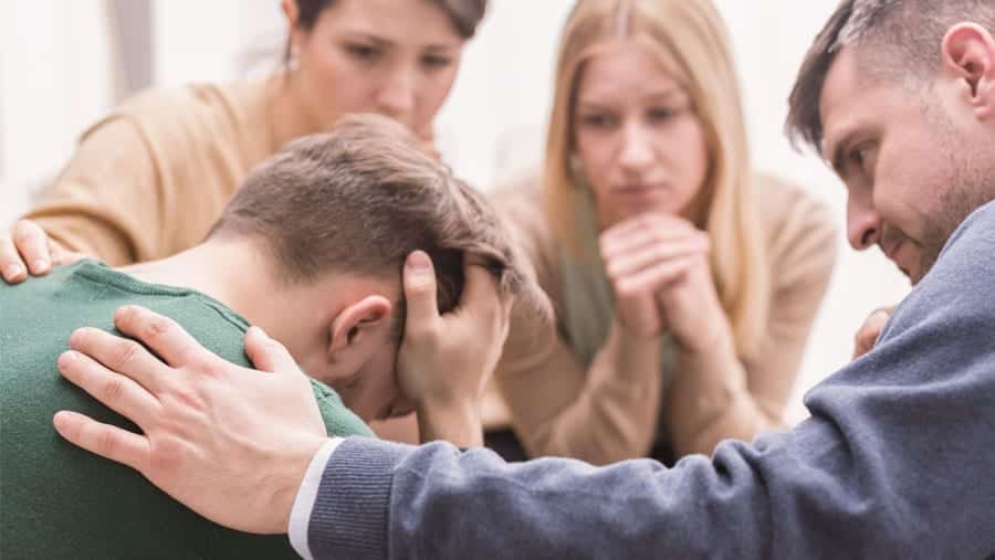 A family of four gathered to provide an intervention for a distressed looking male family member. 