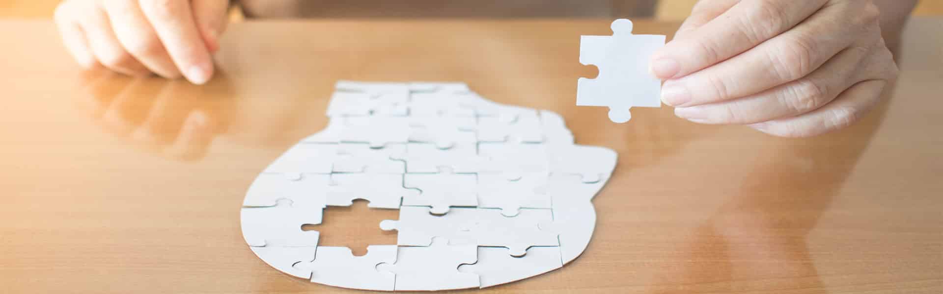 Hands of person doing a puzzle of a head and filling in the missing piece