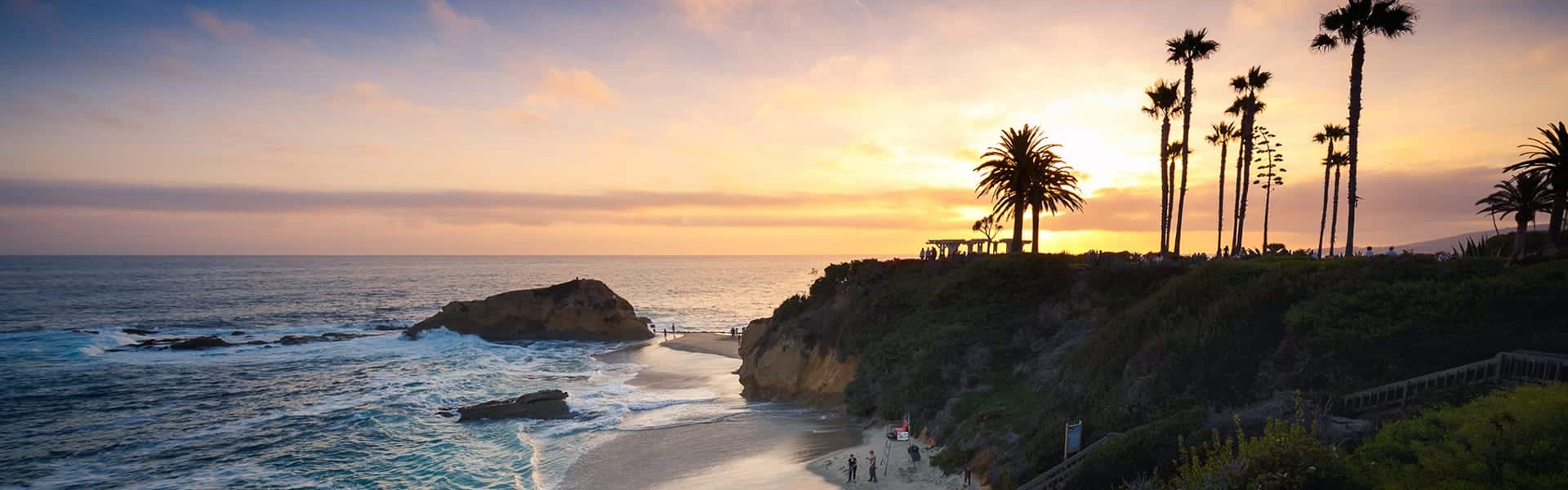 Sun setting on beautiful beach cliffs with warm colors in the sky and profiles of palm trees