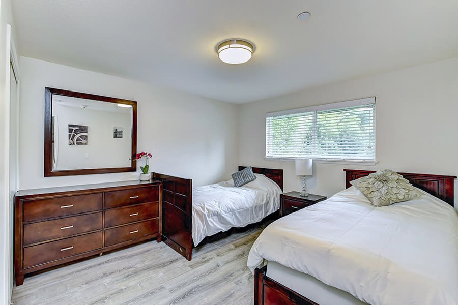 Modern bedroom with double beds, dresser, mirror, wood floors 