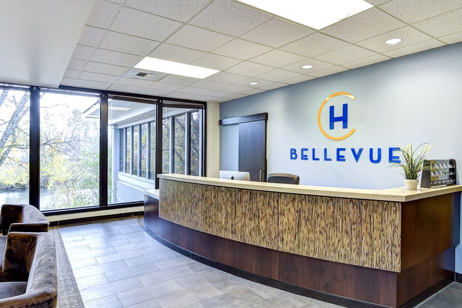 Hotel California Bellevue's front desk with lark windows, brightly lit, with "H Bellevue" logo on the wall