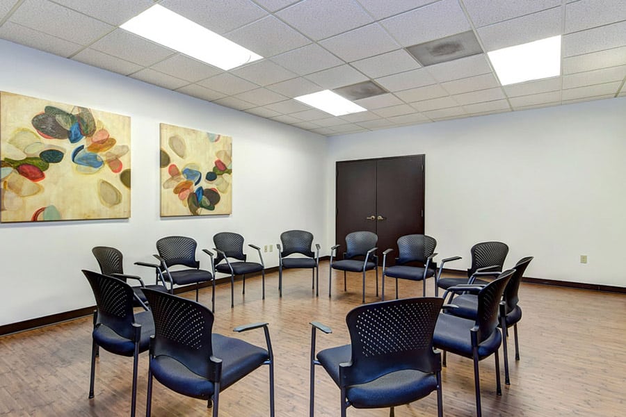 Brightly lit room with paintings on the wall and chairs in circle for group therapy 