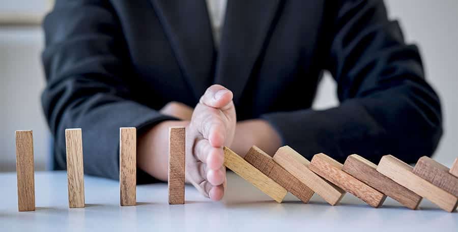 4 Common Triggers For Relapsing On Drugs And Alcohol, man stopping dominoes from falling as an addiction relapse metaphor.