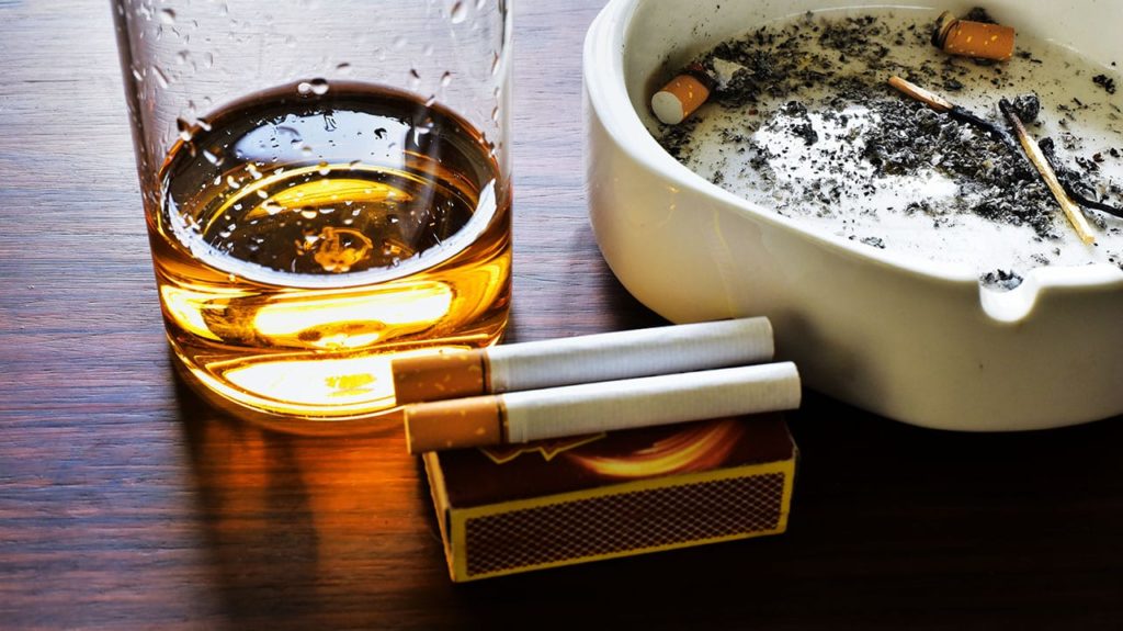 An image of a used ashtray, a cigarette and a glass of alcohol. 