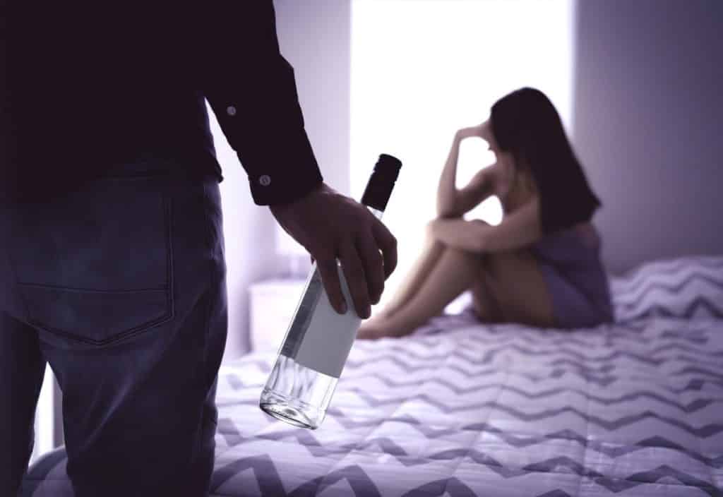 A couple during covid 19 quarantine are confronted about alcohol relapse as the man holds an empty bottle of wine. 