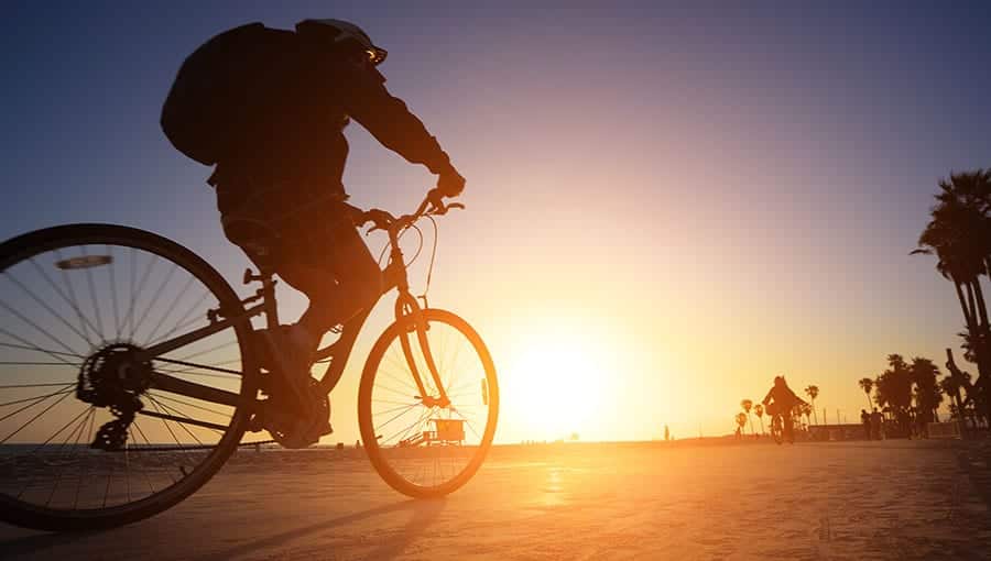 A silhouette of a person riding their bike along the beach. 