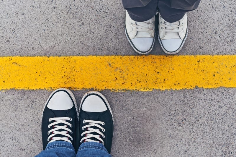 An image of two sets of feet standing on opposite sides of a yellow line is a metaphor for setting boundaries. 