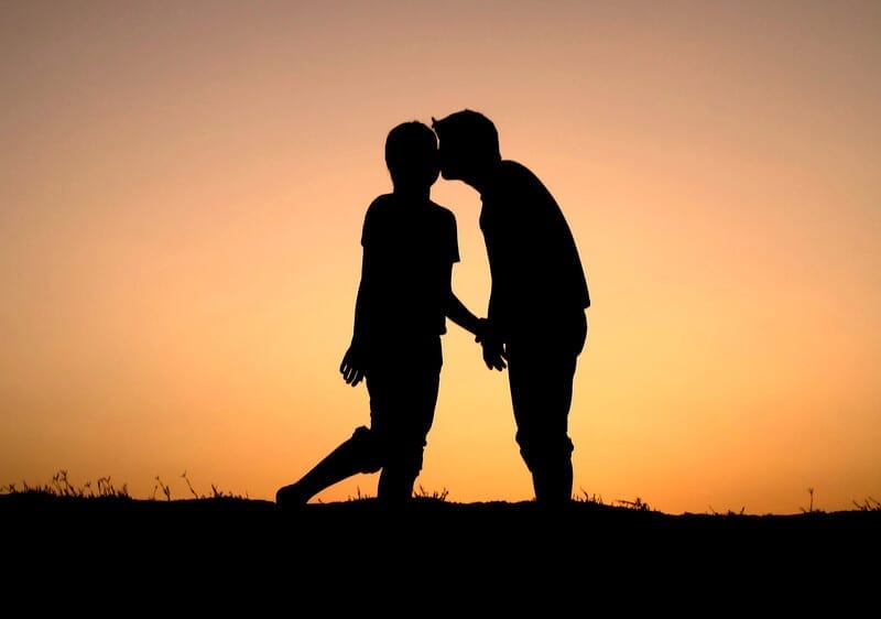 A silhouette of a couple in recovery on a date, kissing in front of a sunset background. 