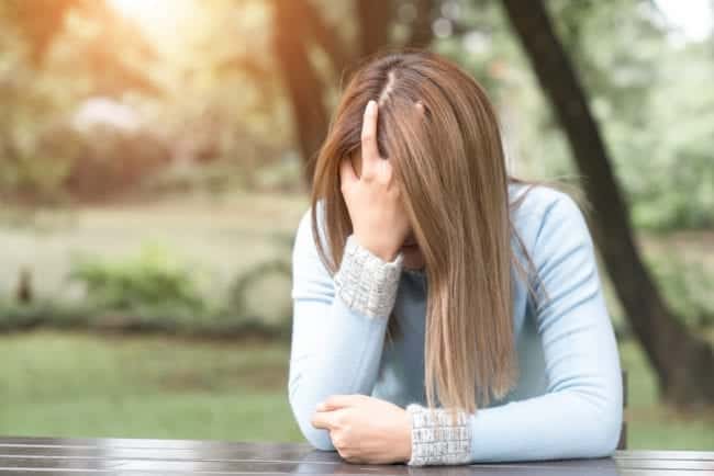 A distressed woman is sitting with her hands on her head contemplating the dangers she faces from self-medicating with drugs and alcohol.