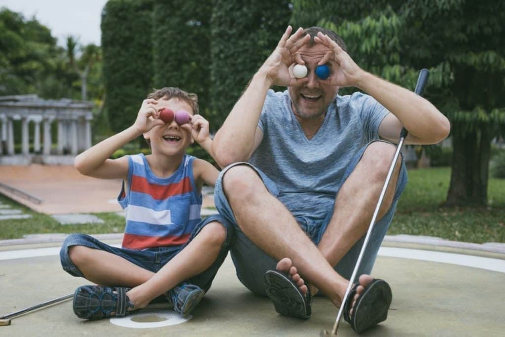 A father and son being silly while playing mini golf with the father having a fun sober night out. 