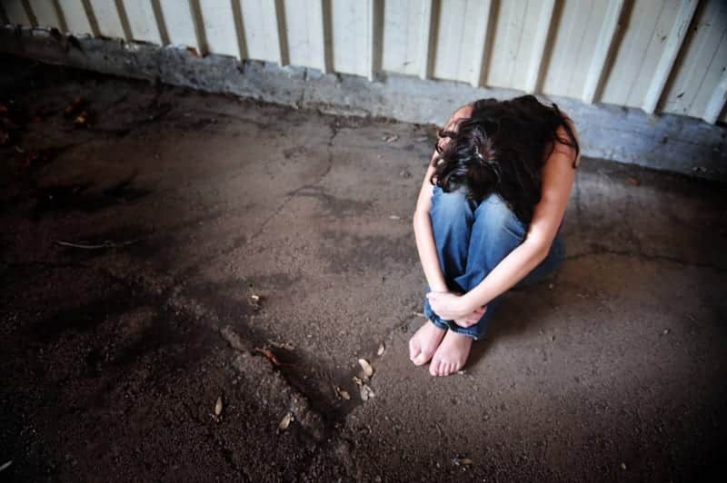 A person addicted to fentanyl sitting barefoot on the street represents the rising risk of fentanyl and the long road to recovery. 