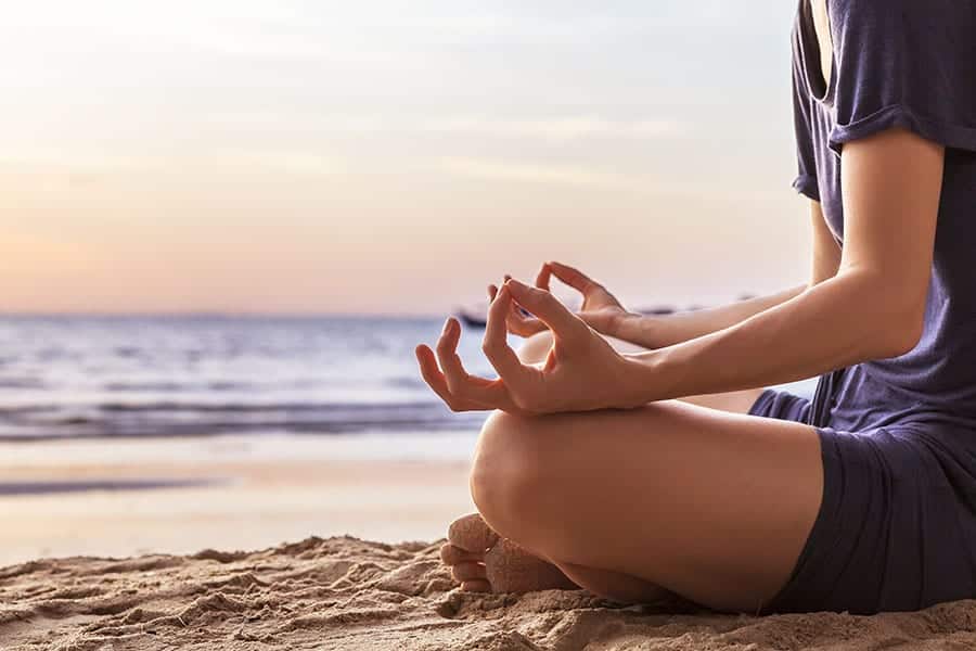 A woman sits on the beach meditating near her choice of drug rehab by the beach.