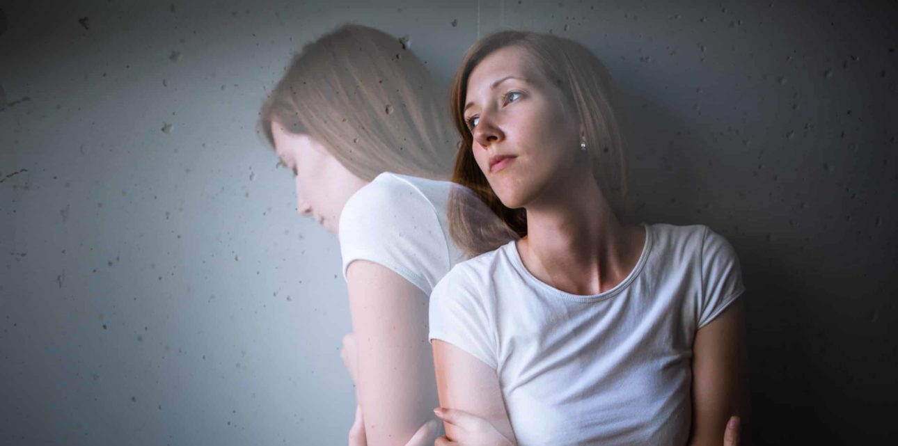 Red haired woman suffering from co-occurring disorder - leaning against wall with another version of her -lighter, opaque turning away