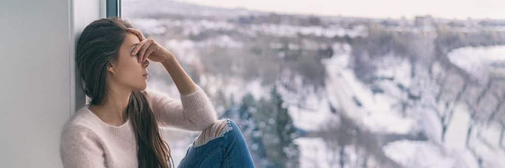 An alcoholic woman grieving and suffering from loss sits by the window. 