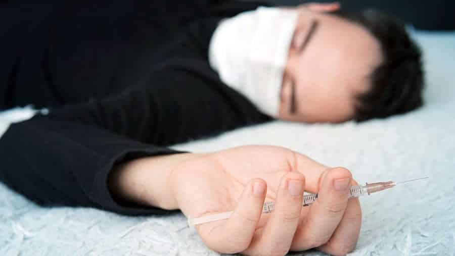 Man overdosing holding an empty syringe while wearing face mask, showing Overdoses Increasing During COVID-19 Pandemic