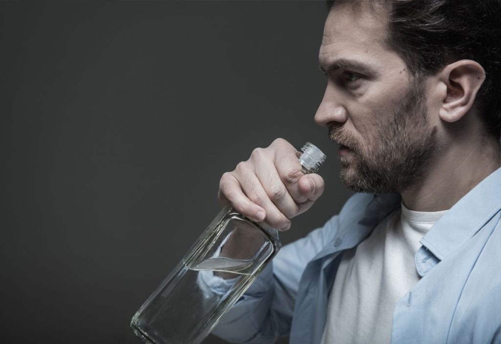 The connections between addiction, grief, and loss shown by man drinking alcohol and grieving.