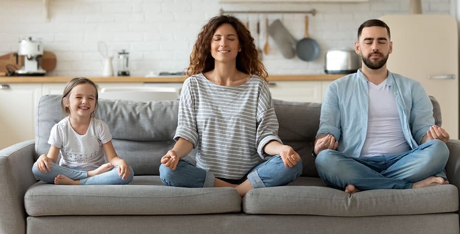 A mother, father and child sit and meditate calmly on the sofa. 