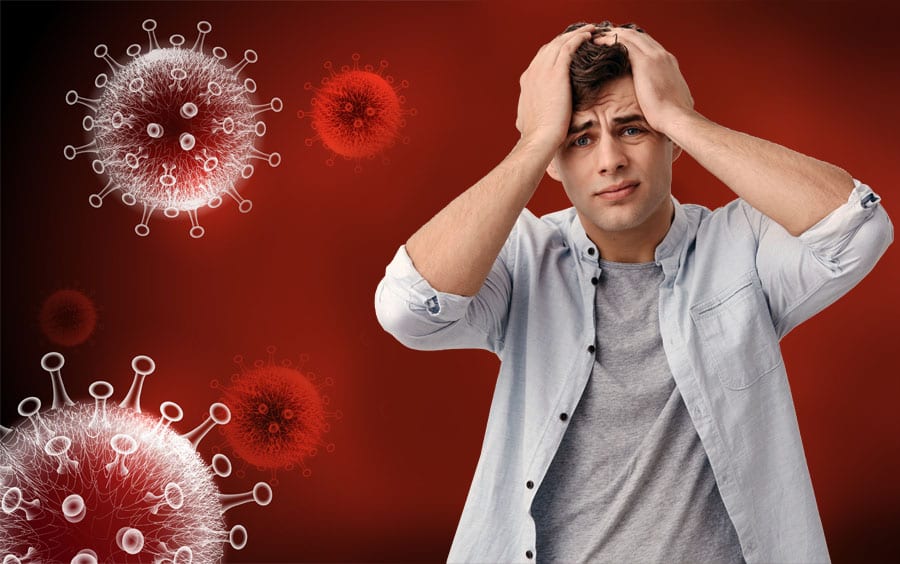 A young man holding his hands to his head surrounded by images of microscopic viruses represents how the Covid 19 virus affecting mental health. 