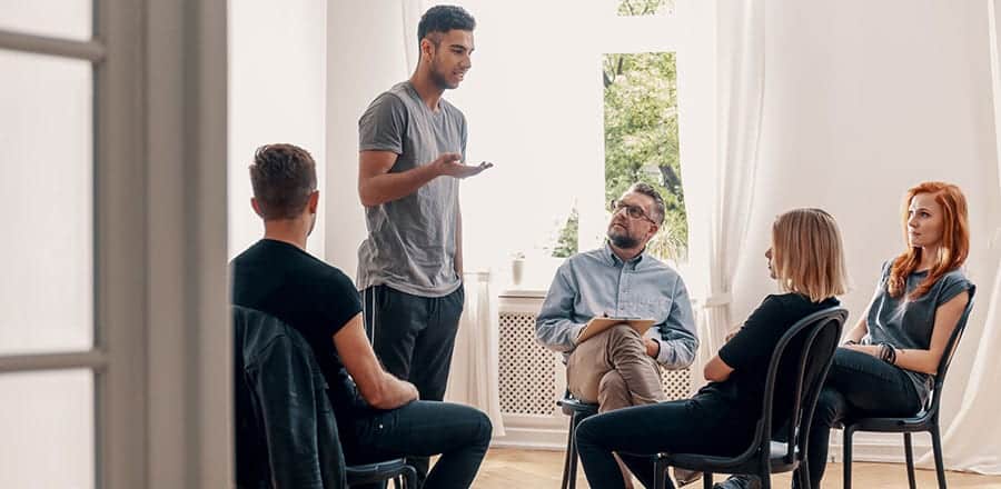 Young adults at an addiction support group meeting discussing questions to ask when choosing a drug rehab center. 