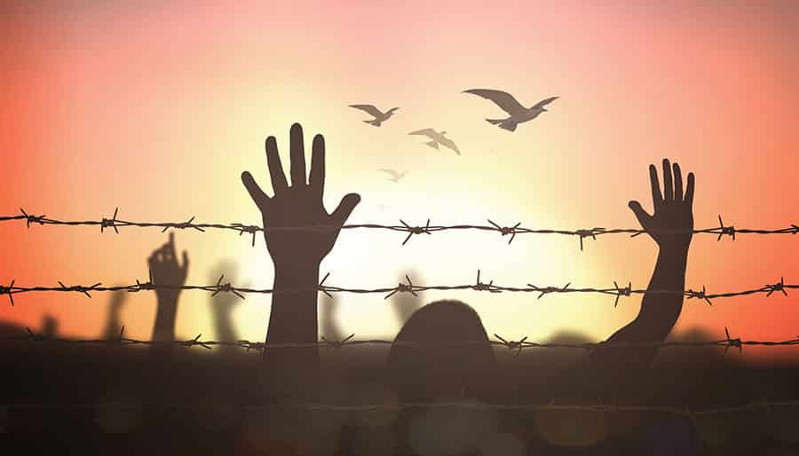 Silhouette of people with their hands in the air behind a prison wall, where a large population could benefit greatly from drug addiction treatment.