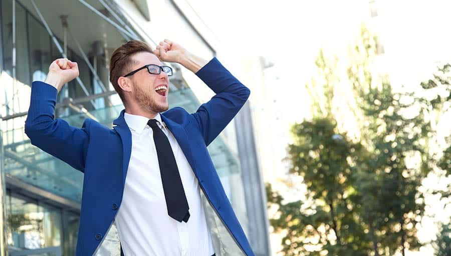 A young man in a suit has his hands in the air in celebration of achieving sobriety. 