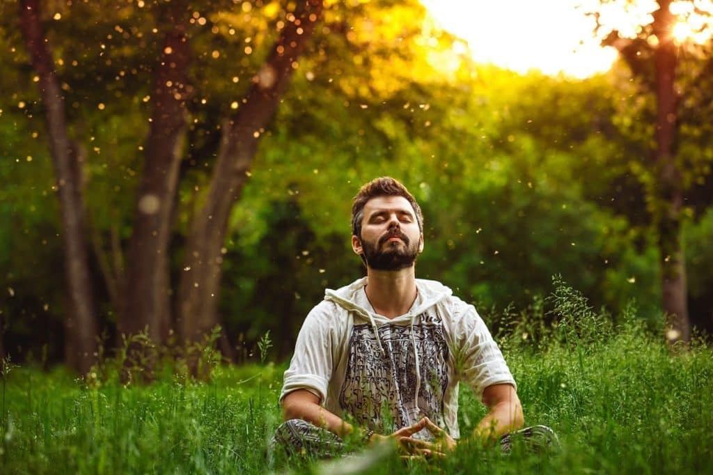 A man is sitting in the middle of the forest meditating as a form of coping with stresses of covid 19. 