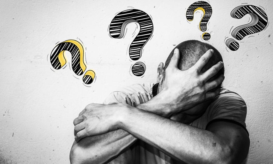 A person with their hand on their head is surrounded by question marks representing questions to consider when choosing a drug rehab center. 
