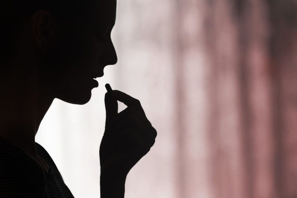 A dark silhouette of a person is taking an opioid pill while experiencing covid 19.