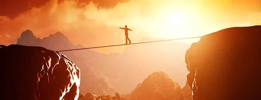 A person walking a tight rope across a mountain canyon. 