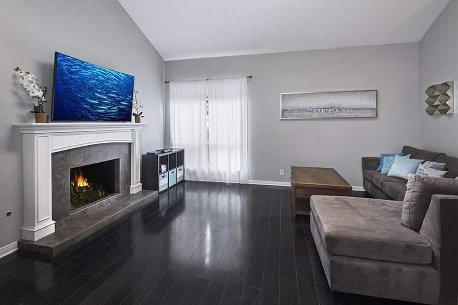 Modern living room with grey couch, fireplace, tv, and hardwood floors in residential rehab