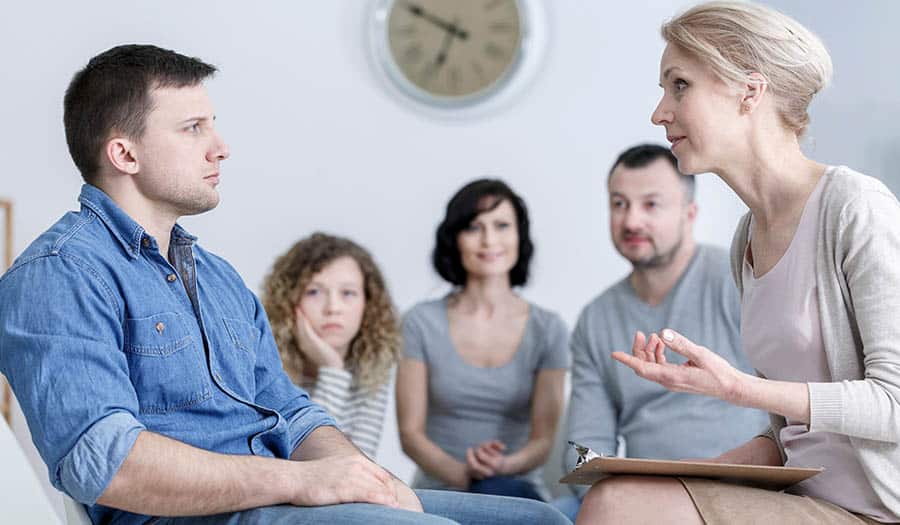 Young man and counselor at rehab engage in group discussion about drug addiction and recovery.