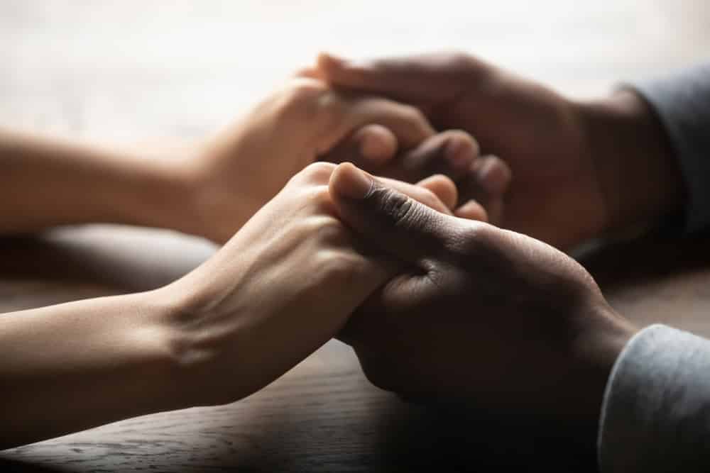 Paid of hands holding another pair of hands resting on wood table