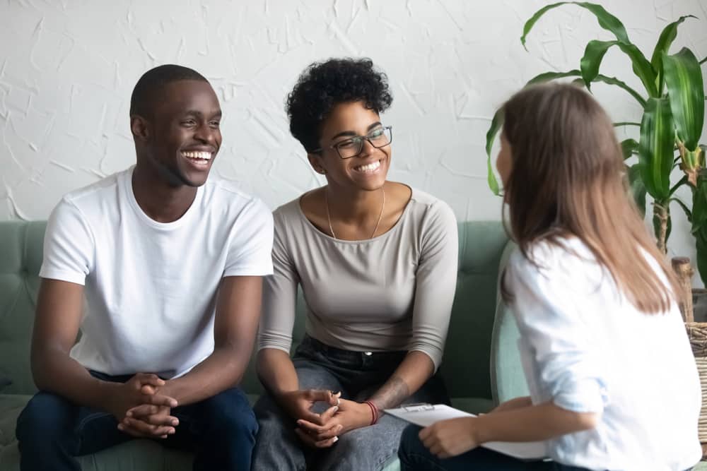 Smiling couple sitting on couch in front of counselor with notepad