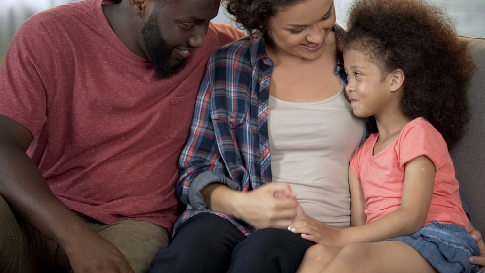 Smiling parents sitting on couch with mom holding little girl 