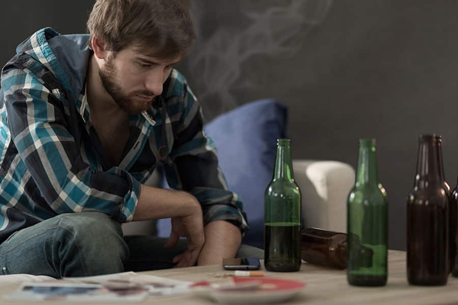 A man sitting on the sofa contemplates if he has been drinking too much during the covid 19 pandemic. 