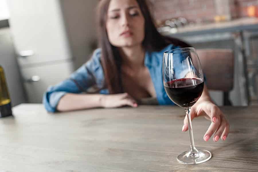 An intoxicated woman reaches across the table for a glass of wine.  