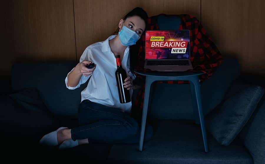 A woman is holding a bottle of wine while watching breaking news about how women are dying of alcoholism during covid 19.