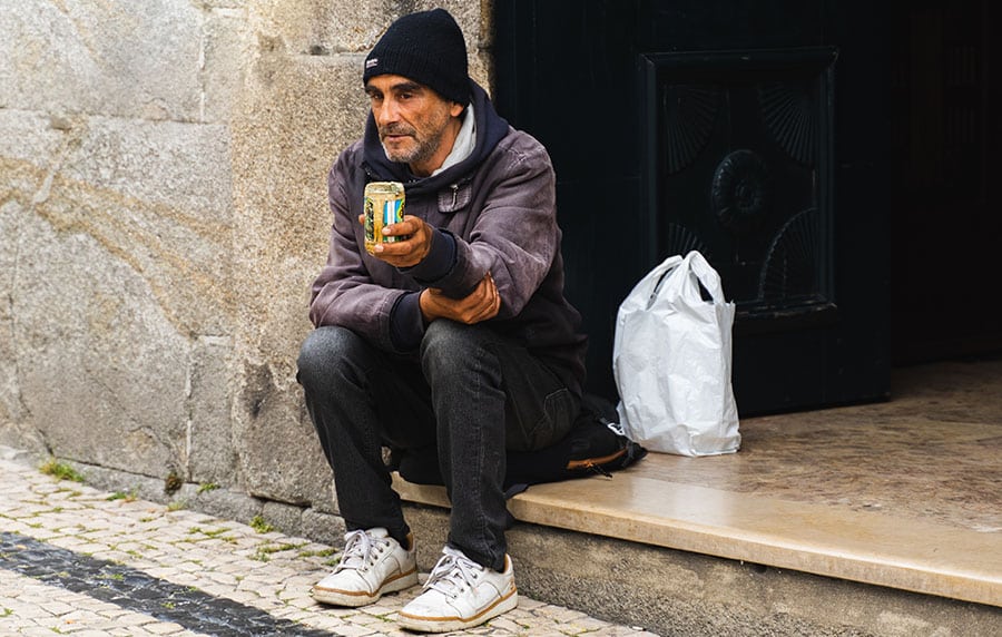 A man suffering from addiction sits on a street curb holding an empty can.