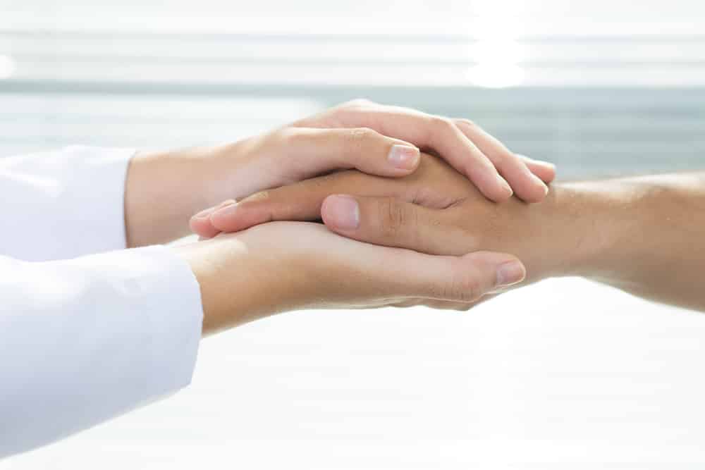 Hands in wearing lab coat holding older, male hand