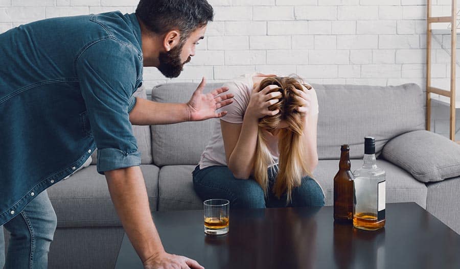 A woman suffering from alcoholism holds her hands on her head after drinking too much and is being scolded by a male counterpart. 