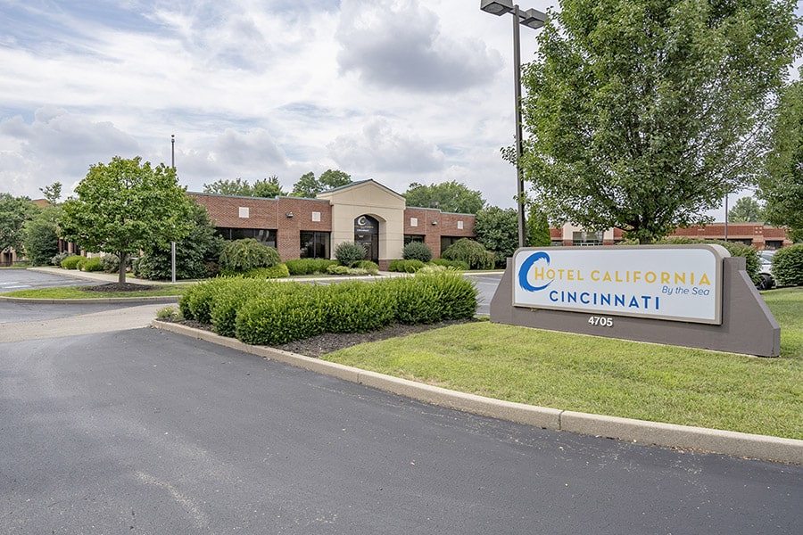 Clean, clear view of Hotel California by the Sea's Cincinnati locations outpatient building. Cloudy, bright day with green grass and trees. The HCBTS Logo in the forefront 