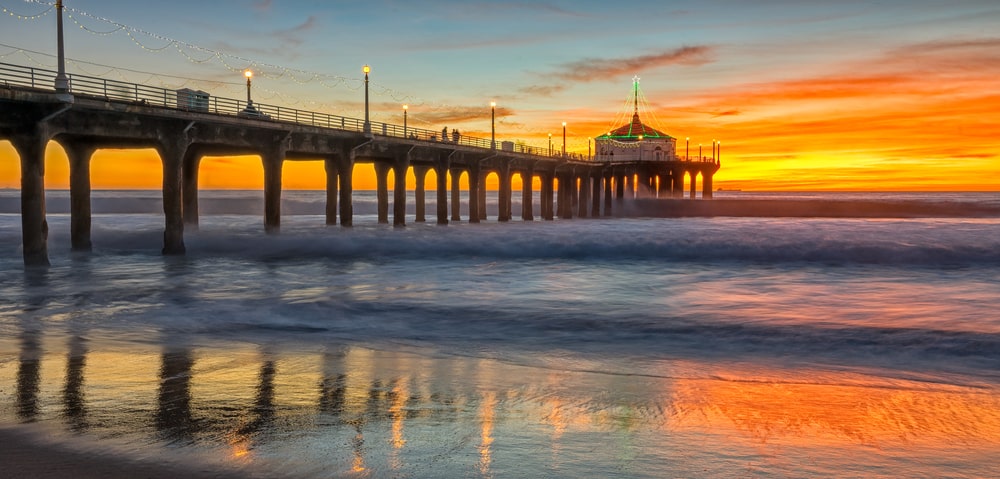 Pier stretching out into the ocean with beautiful sunset lighting up the sky and waves reflecting the orange hues