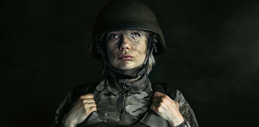 A female veteran dressed in military gear out in the field contemplates the connection between PTSD and addiction. 