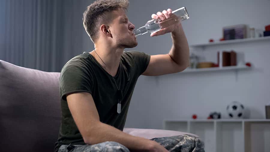 PTSD and Alcohol Addiction - Man in military uniform drinking alcohol, relationship between PTSD and Addiction.