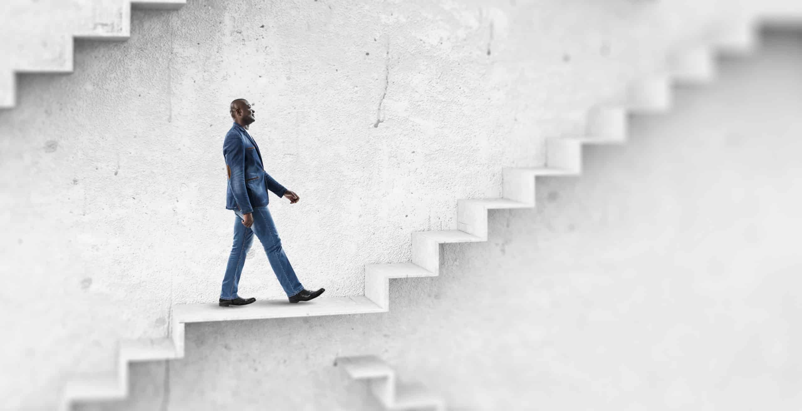 tall man wearing a denim blazer looking up, walking up white stairs