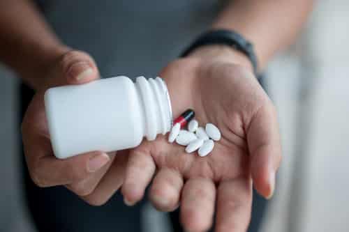 Hands outreached, palm facing upward with other hand dumping pills from a bottle in it 